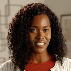 Woman with curly hair wearing a red top and white cardigan indoors