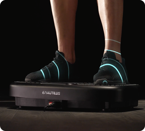 Person using a Nautilus vibration plate on a dark background